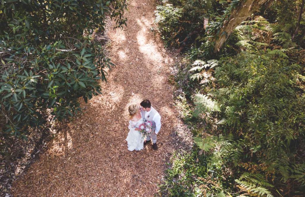 aerial drone photography of bride and groom on beach pathway