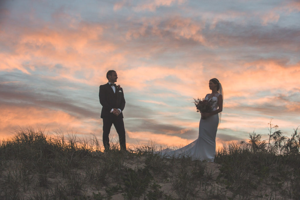 bride and groom silhouetted against beach sunset photo