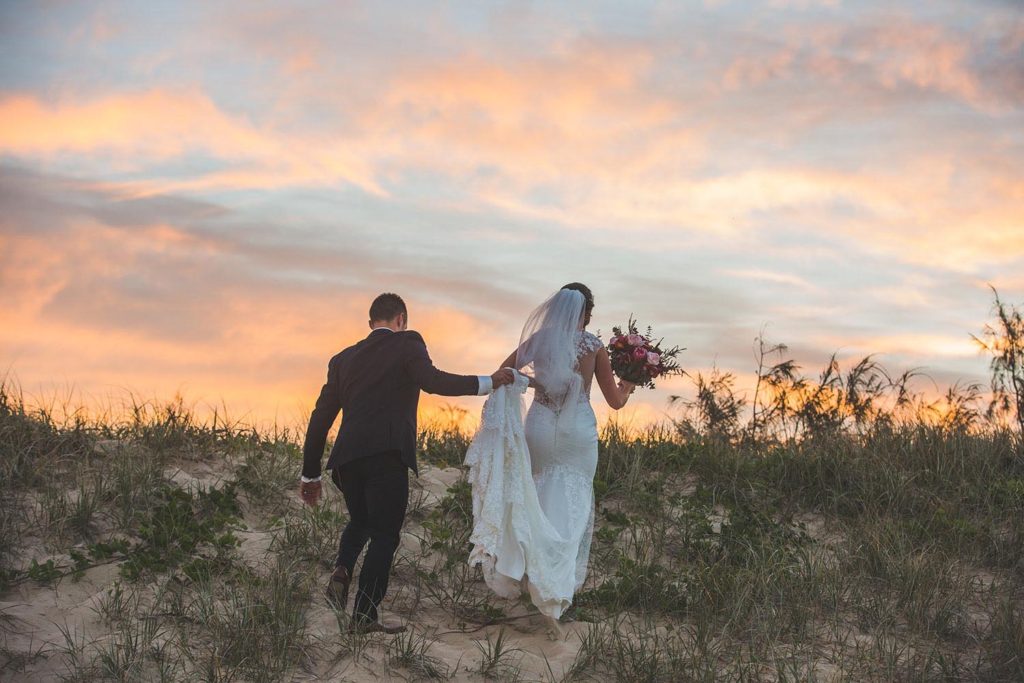 bride and groom walking on beach at sunset