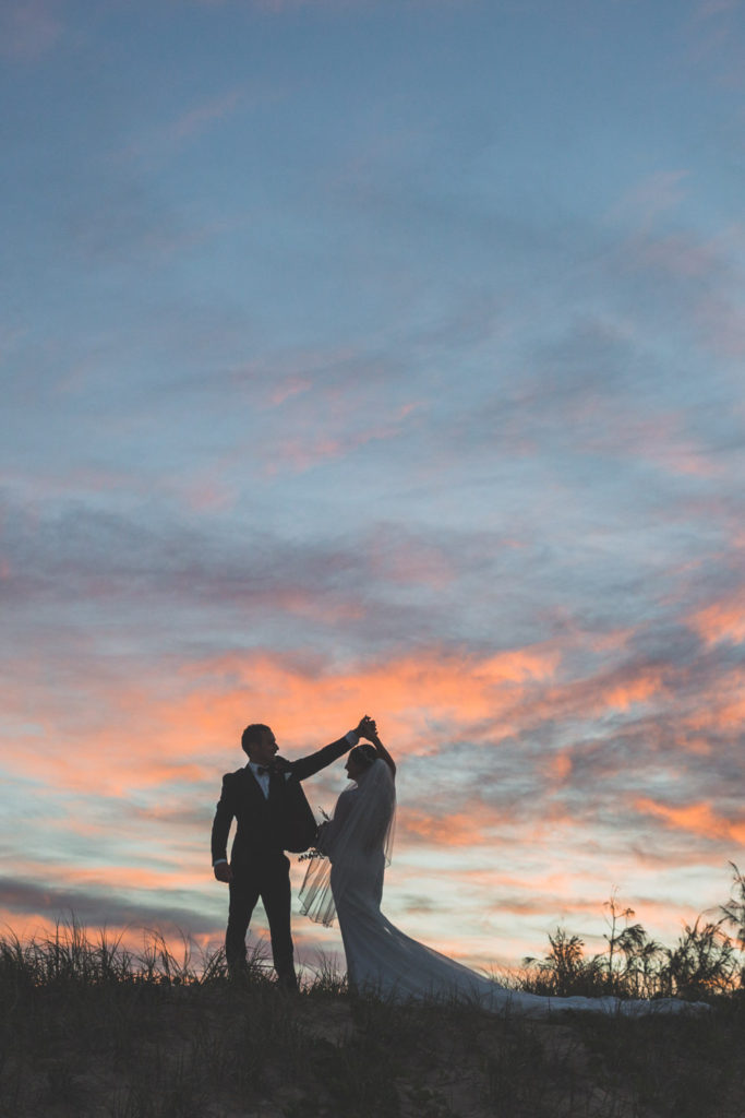 fun bride and groom silhouetted against beach sunset photo