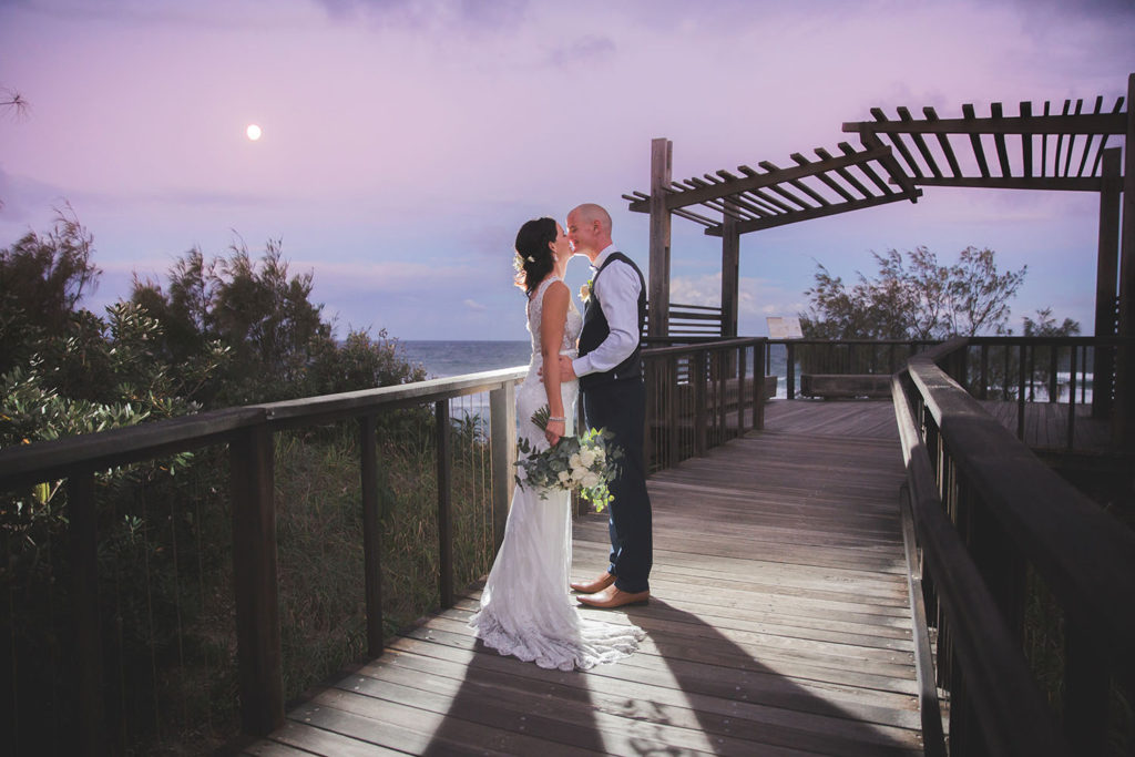night photography of bride and groom by coast with moon