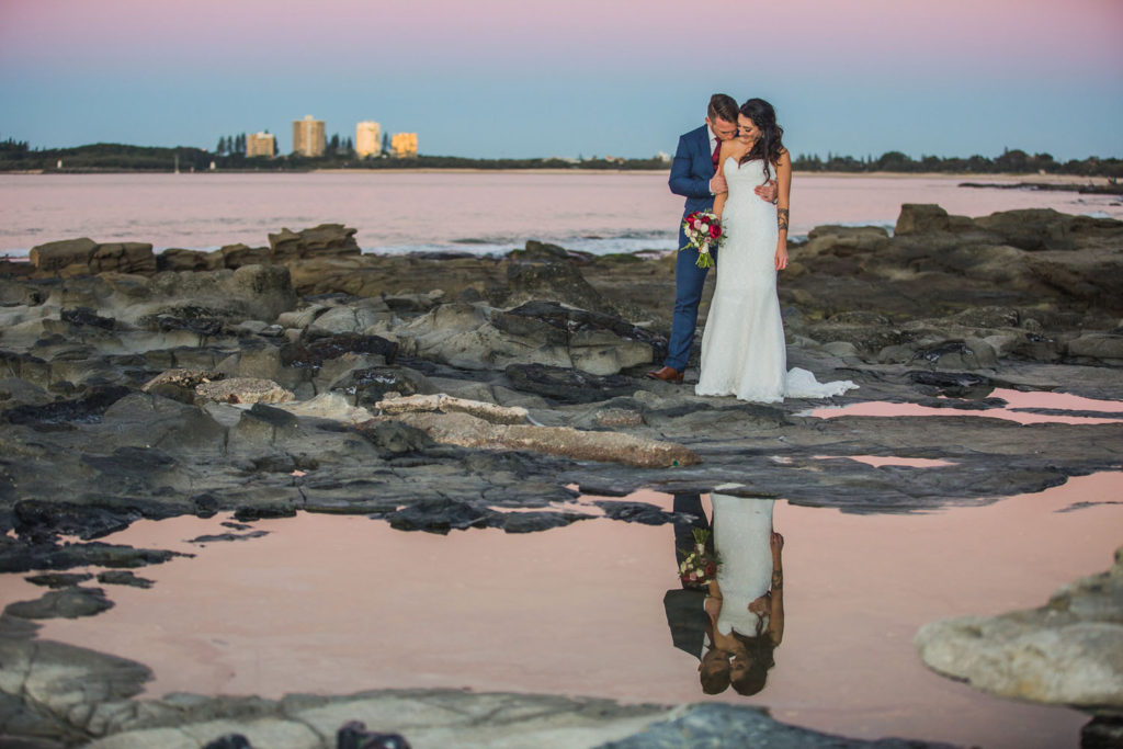 photograph of bride and groom at beach at sunset with reflection in water