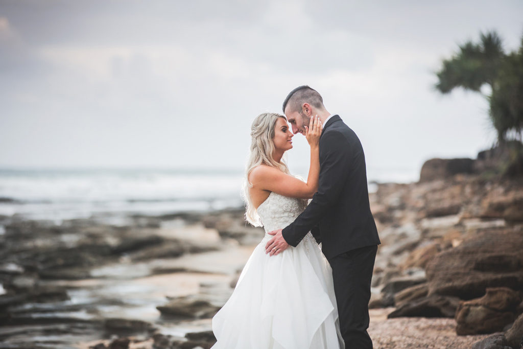 photograph of wedding couple on rocky beach with clouds